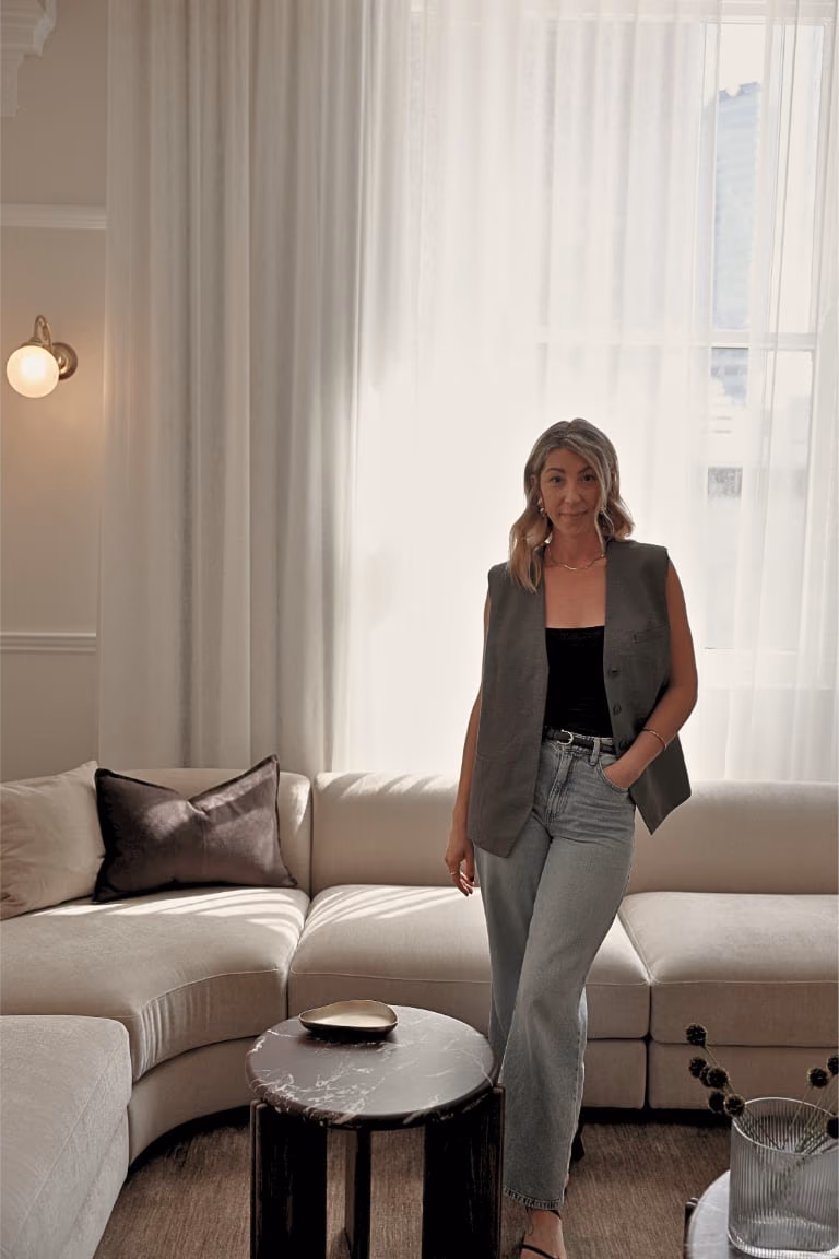Elisha standing in front of a cream sofa and sheer curtains