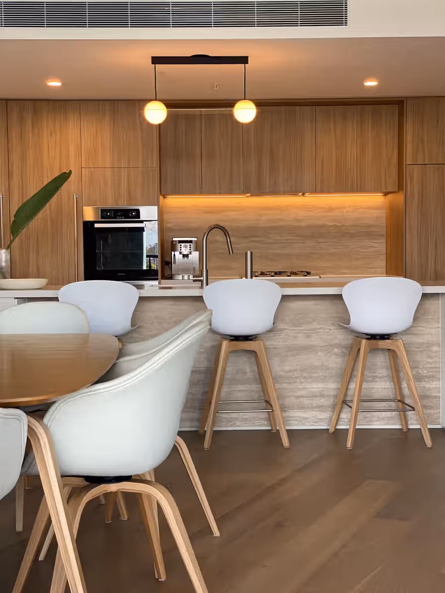 Walnut kitchen with a stone island, white bar stools and a slim black pendant