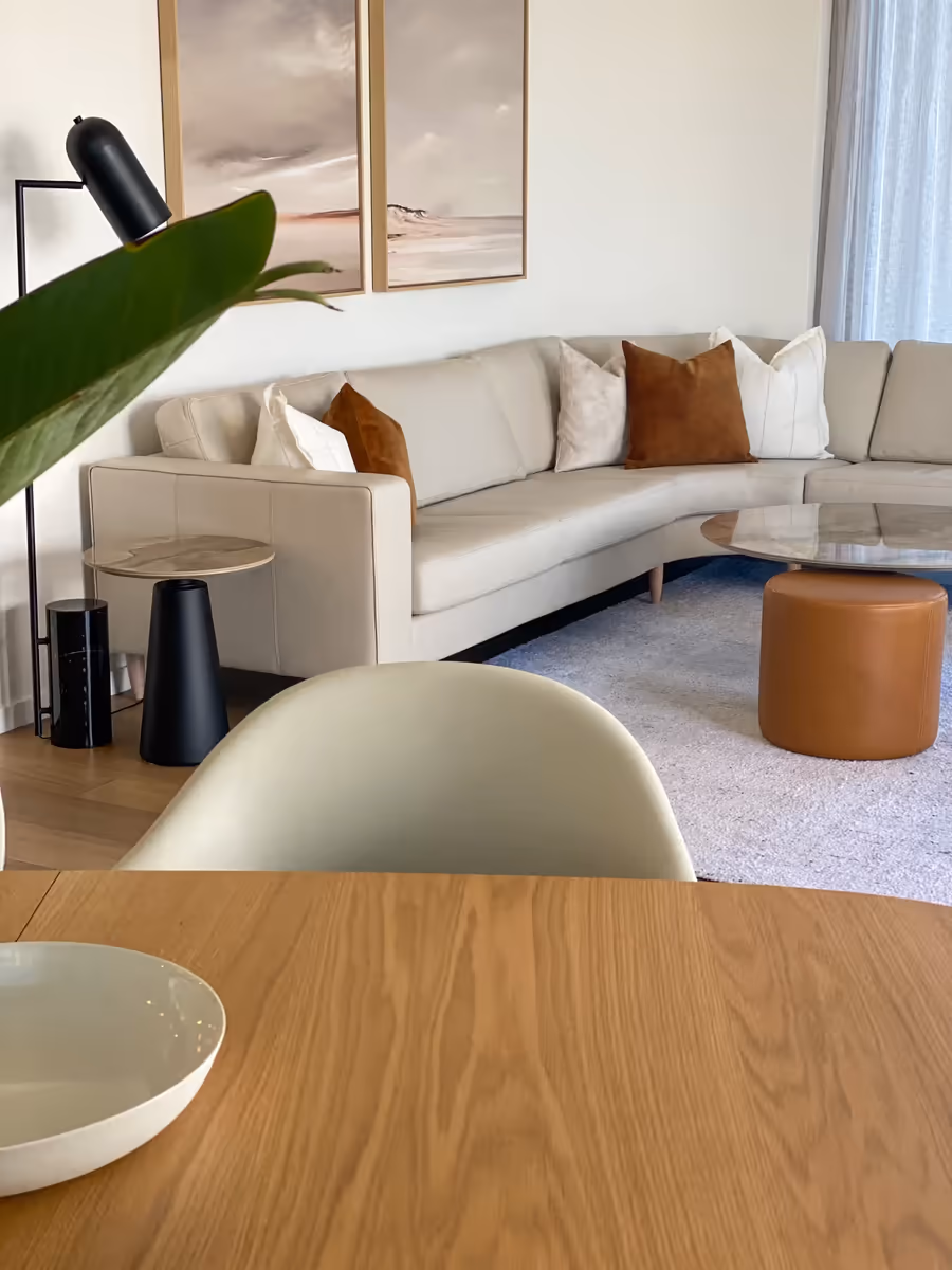 Oak dining table in the foreground, with the cream sofa and tan leather ottoman beyond