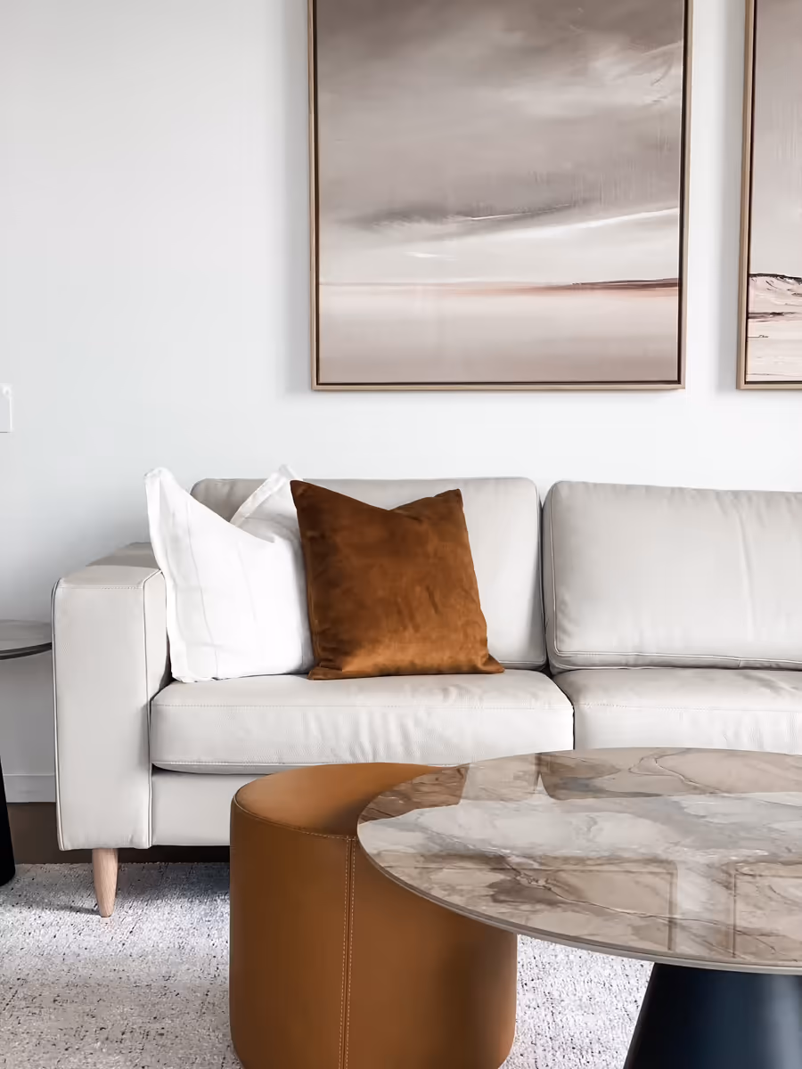 Cream sofa layered with tan and white cushions beneath a soft abstract canvas
