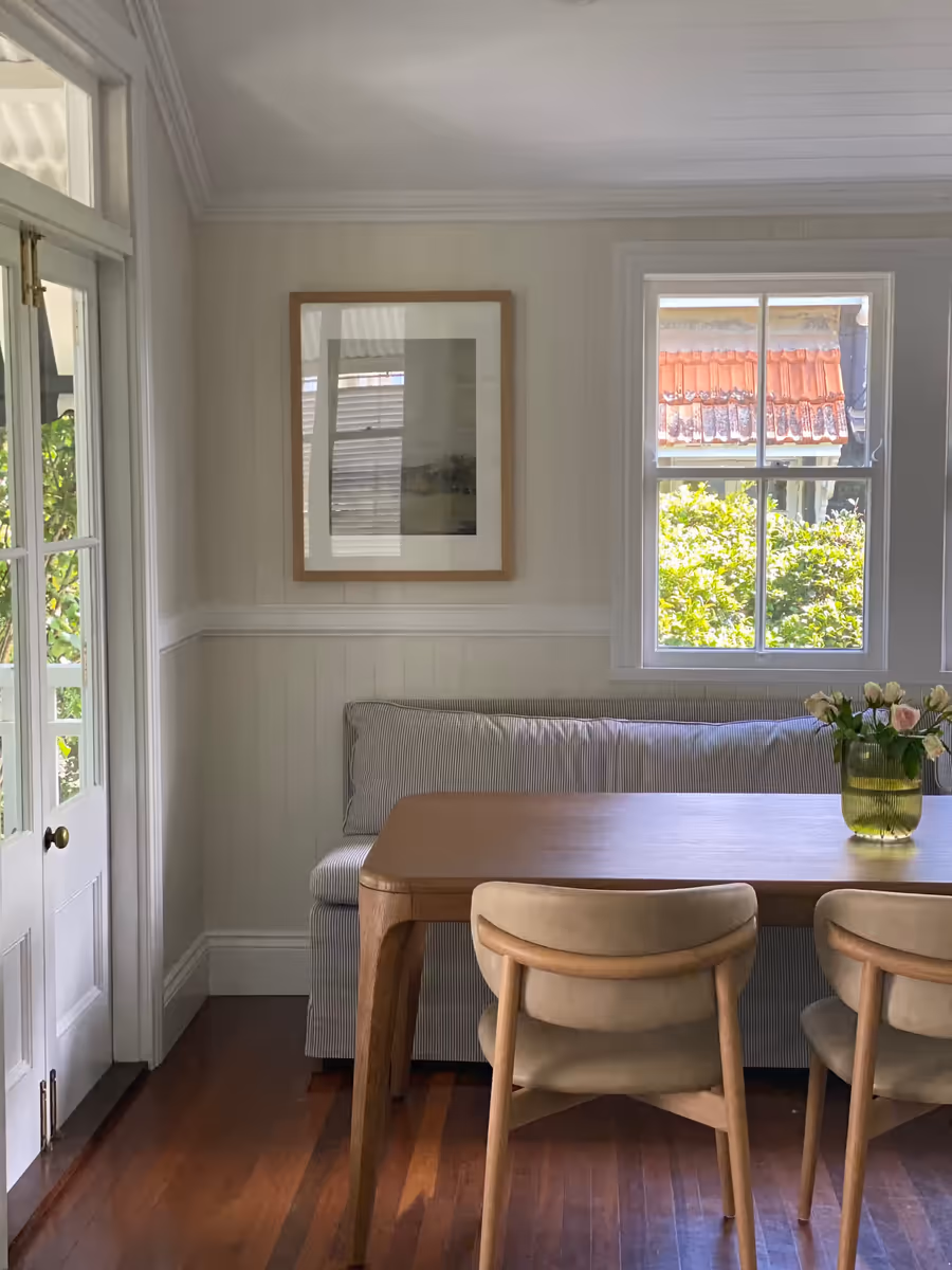 Oak dining table and curved-back chairs beside a built-in banquette under a sash window