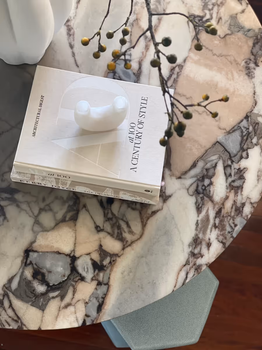 Design books and a marble bird resting on a round Calacatta Viola table top