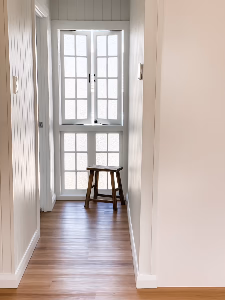 Panelled hallway leading to a casement window with a timber stool beneath it