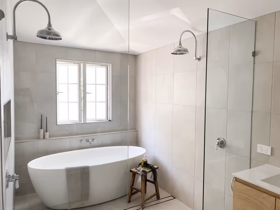 Freestanding bath under the window, with twin gooseneck showers behind a glass screen