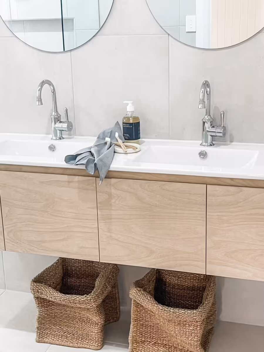 Twin basins on a pale timber vanity below round mirrors, baskets stowed underneath