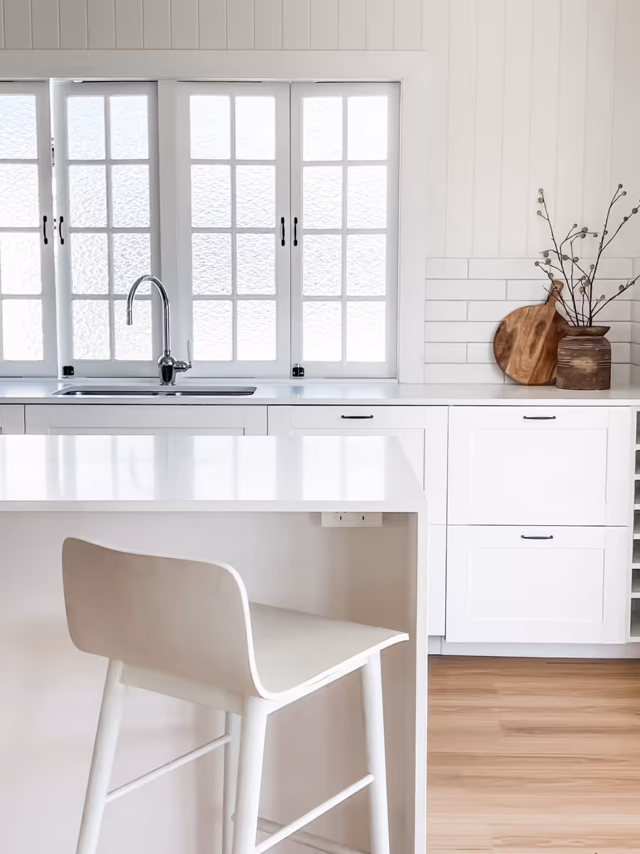 White shaker kitchen with a stone benchtop and a pale bar stool pulled up to the breakfast bar