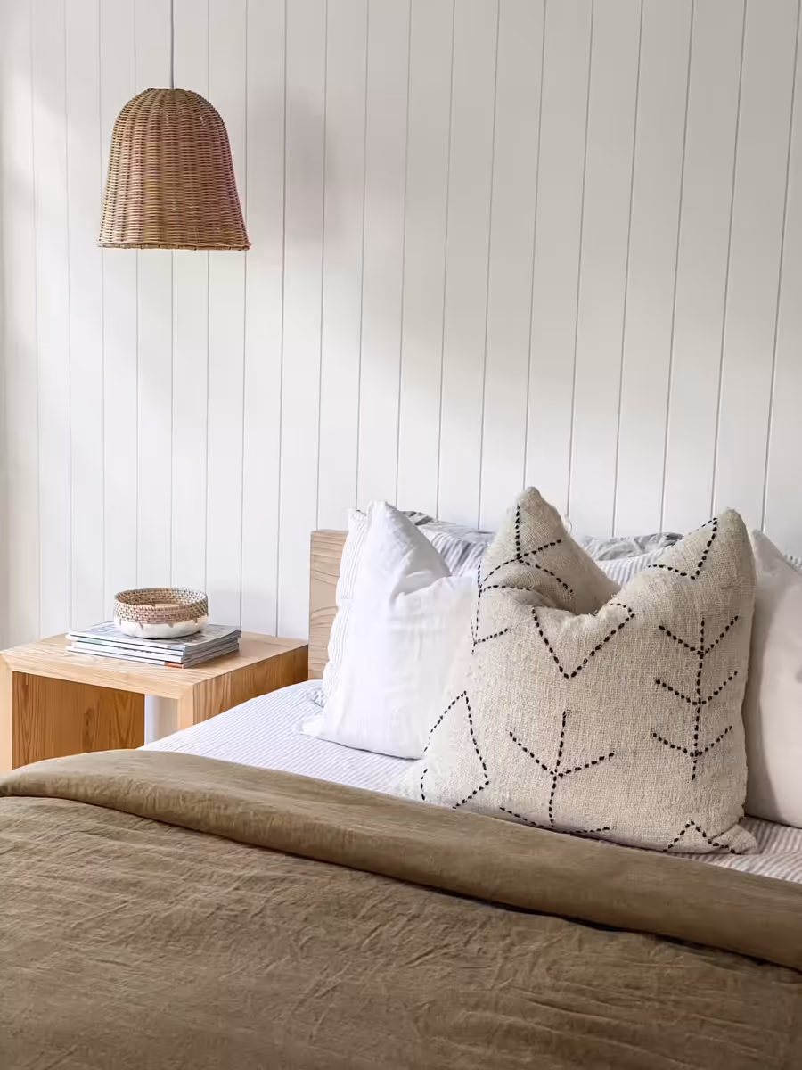 Olive linen bedding and embroidered cushions below a rattan pendant
