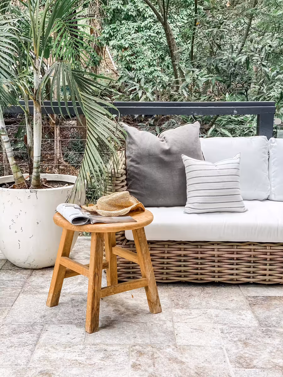 Cushioned wicker daybed and a timber stool on the travertine terrace, backed by palms
