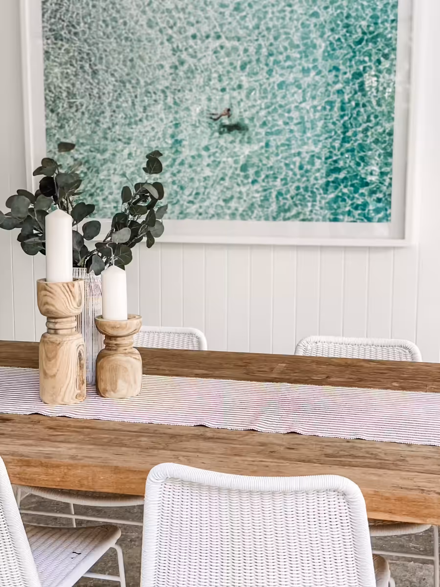 Recycled timber dining table and white rattan chairs below an aerial print of the ocean