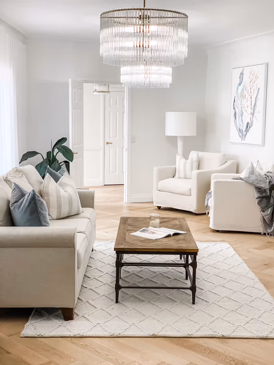 Formal lounge with a tiered glass chandelier, cream armchairs and a patterned rug on parquet