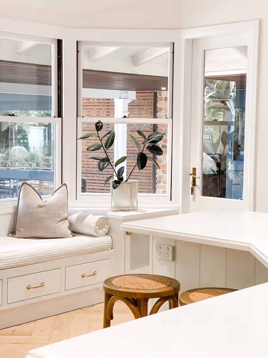 Cushioned window seat in the bay window, with rattan stools at the kitchen bench