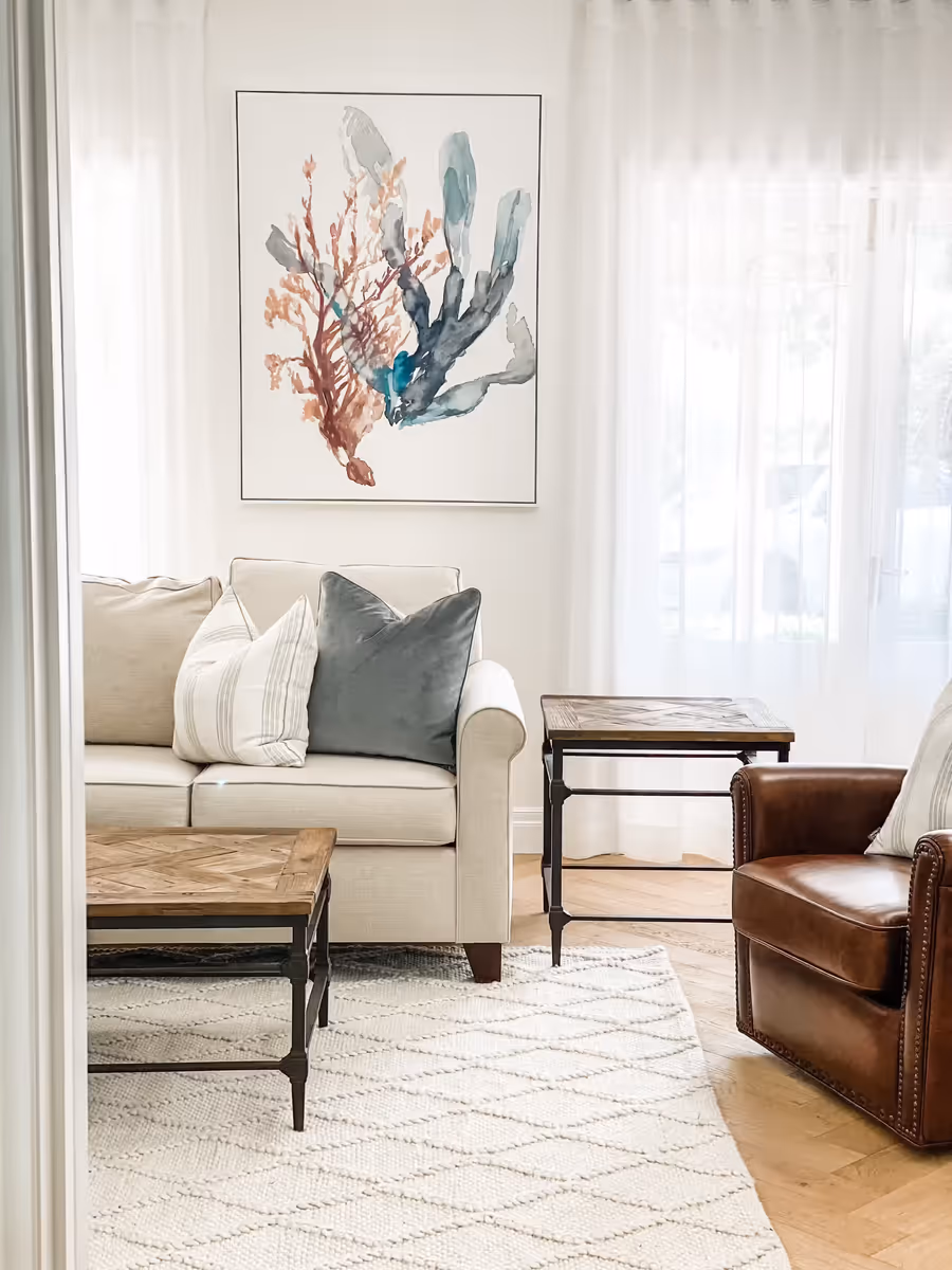Cream sofa and a tan leather club chair around a timber coffee table, below a coral print