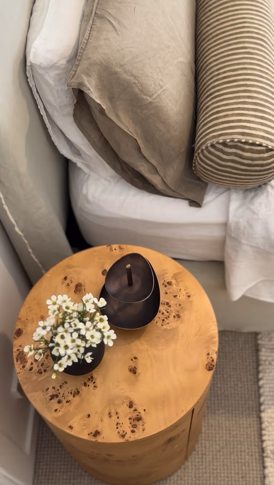 Burl timber bedside table holding a black vessel and a posy of white blossom