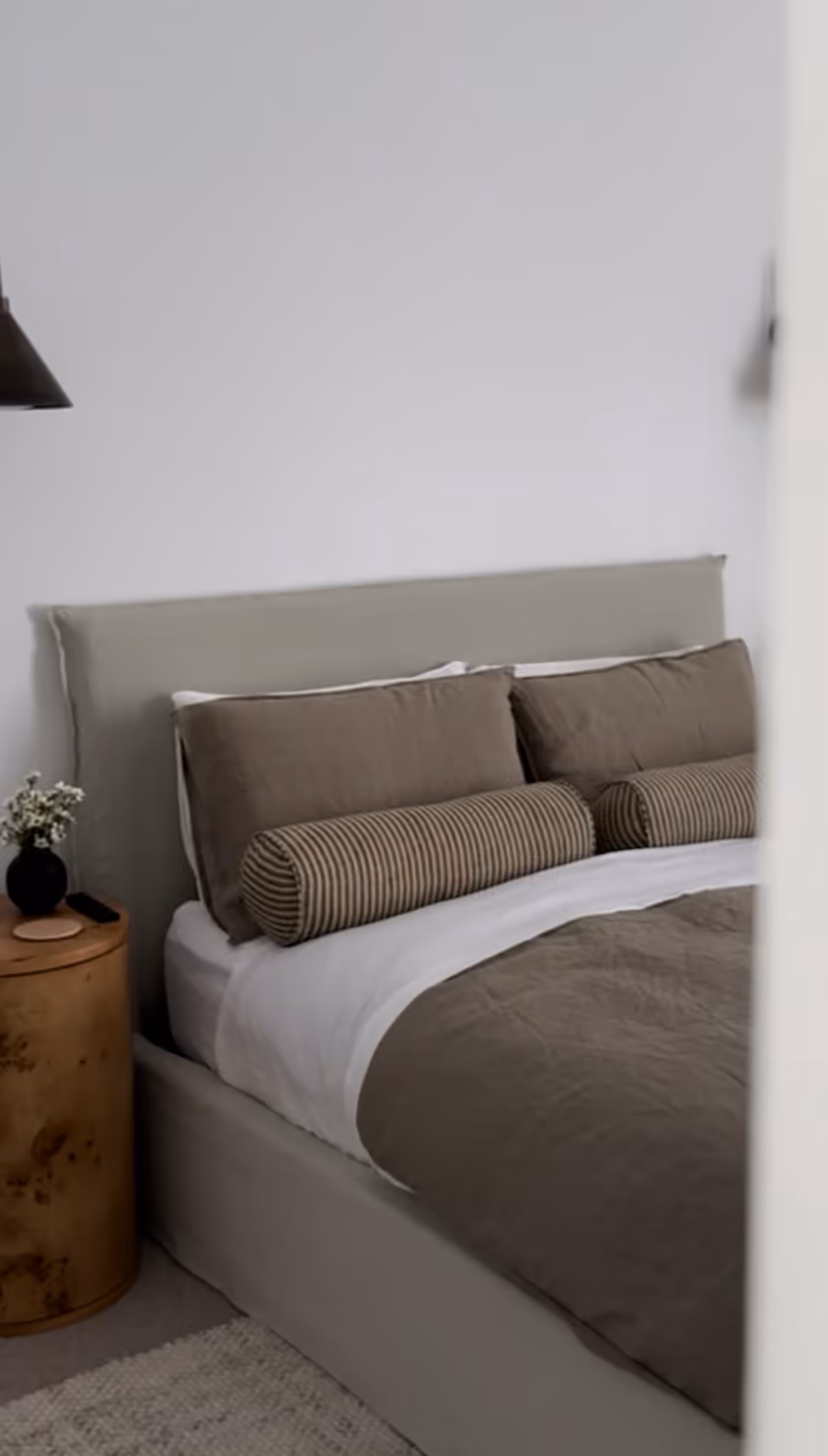 Upholstered bed dressed in olive linen, beside a burl timber bedside table