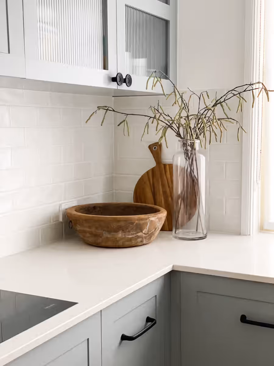 Timber dough bowl and a glass vase on the benchtop, under fluted glass cabinetry