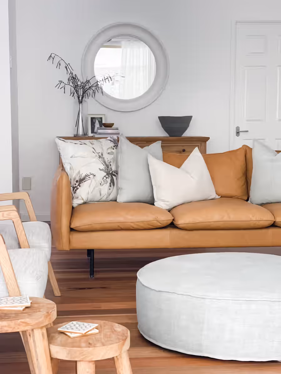 Tan leather sofa and a pale round ottoman below a porthole mirror