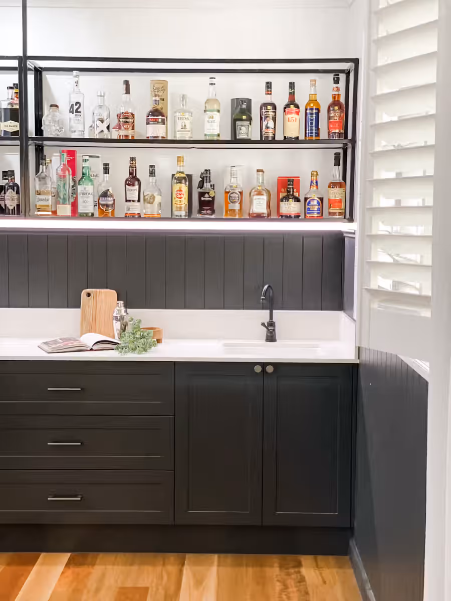 Home bar with backlit spirits shelving above dark green panelled joinery