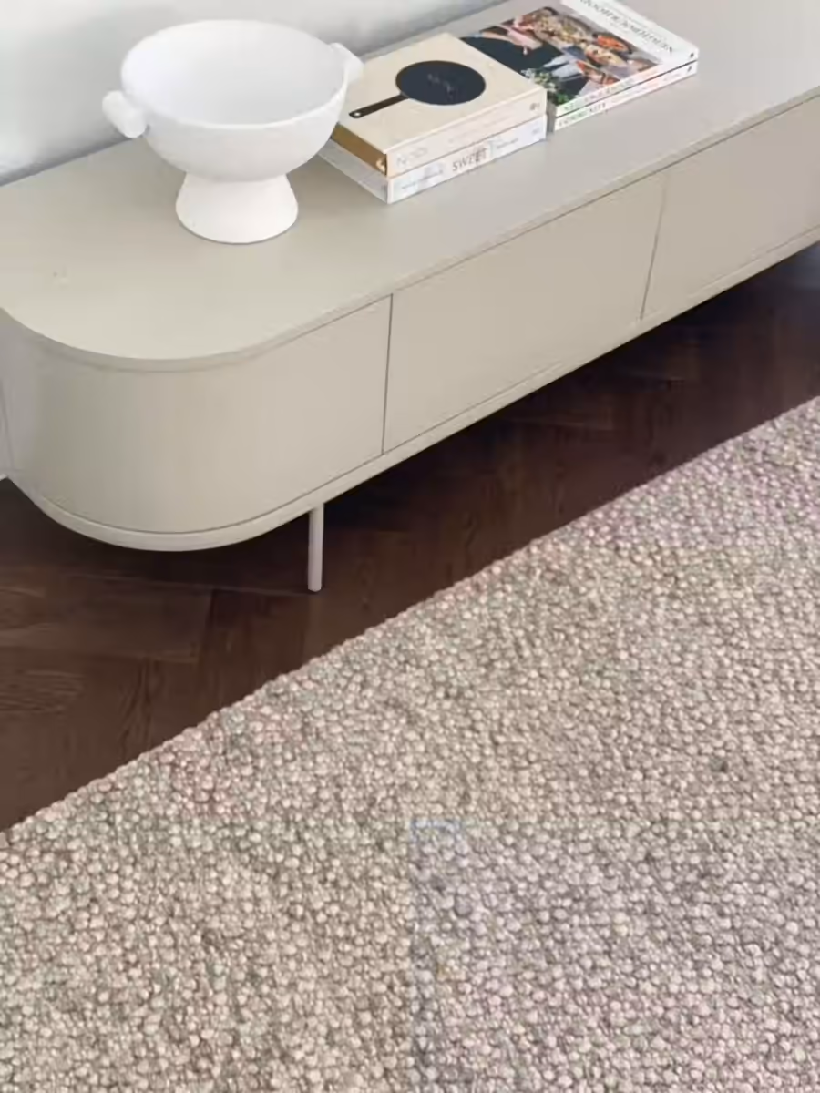 Curved cream media unit on herringbone floors, topped with a pedestal bowl and books