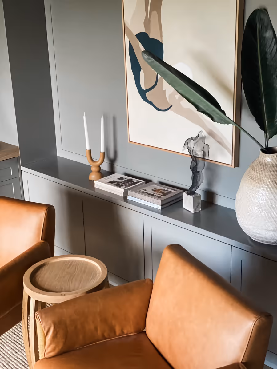 Tan leather armchairs against dark green joinery, below a large abstract canvas
