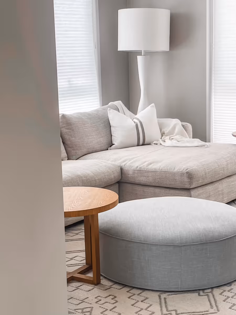 Linen corner sofa and a round ottoman under a tall white floor lamp