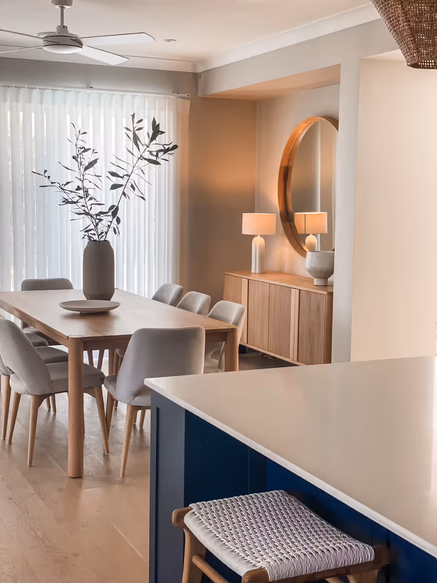 Oak dining table and grey chairs beside the navy island, a round mirror above the sideboard