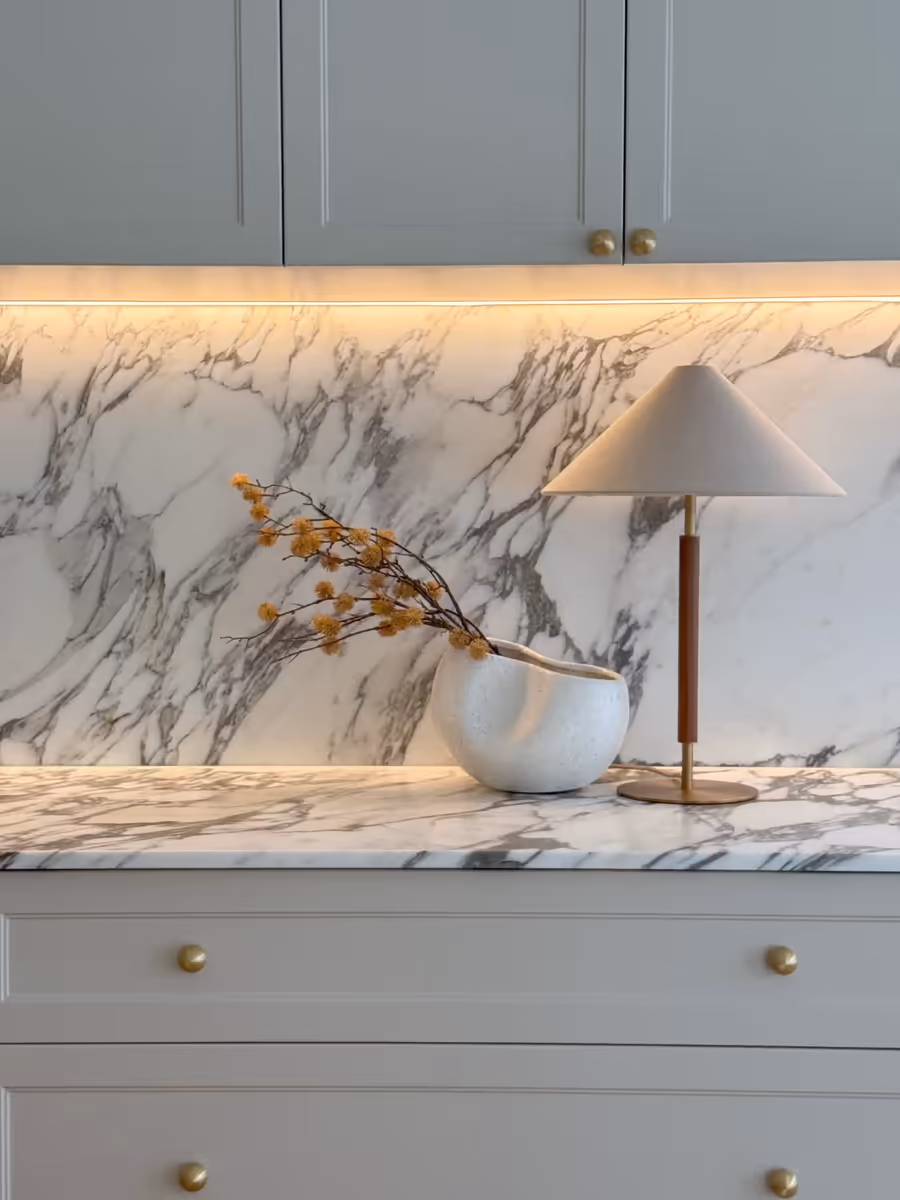 Marble splashback lit from beneath the cabinetry, with a lamp and berry stems on the bench