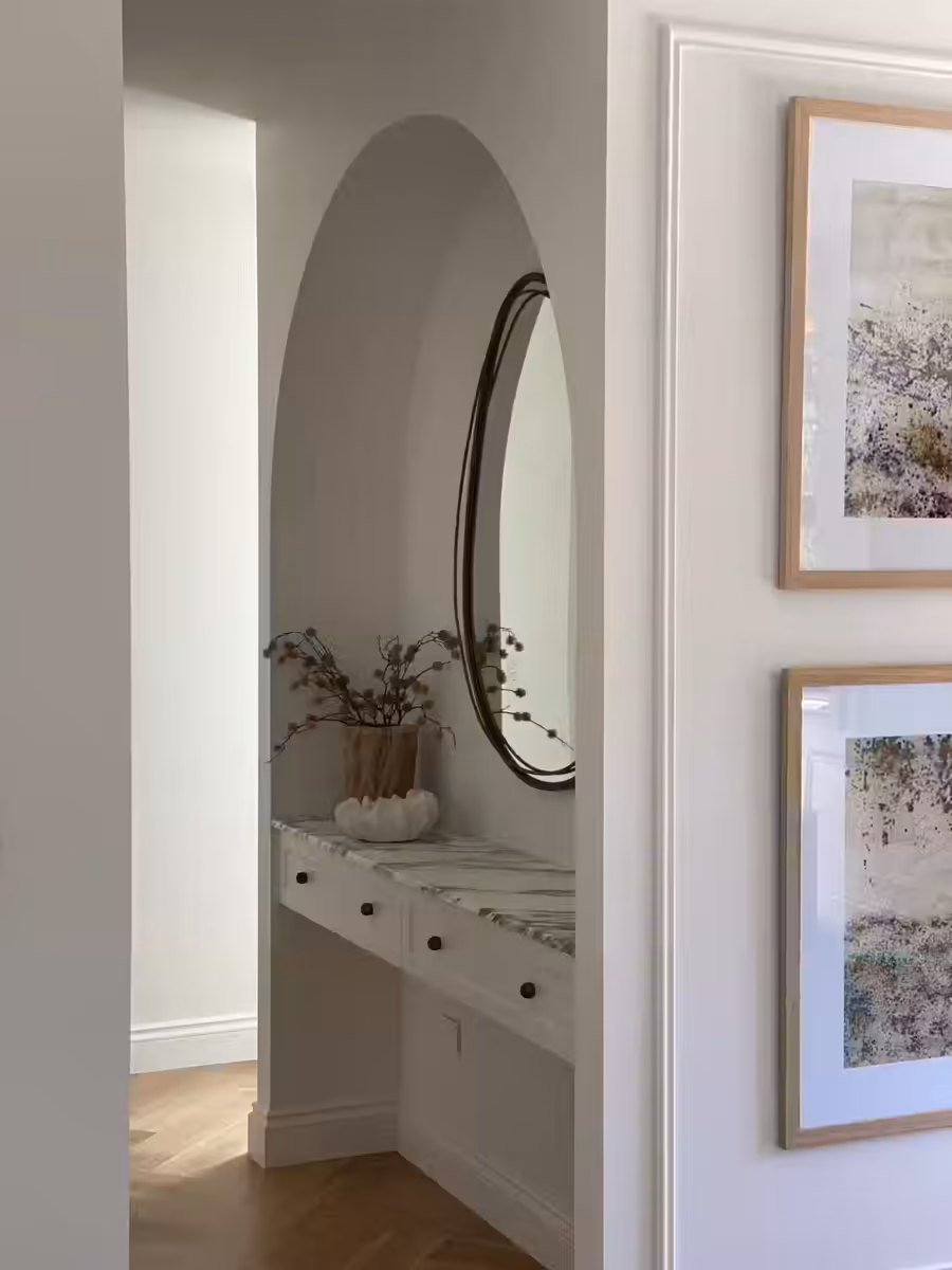 Arched niche holding a marble-topped dressing table below a round mirror