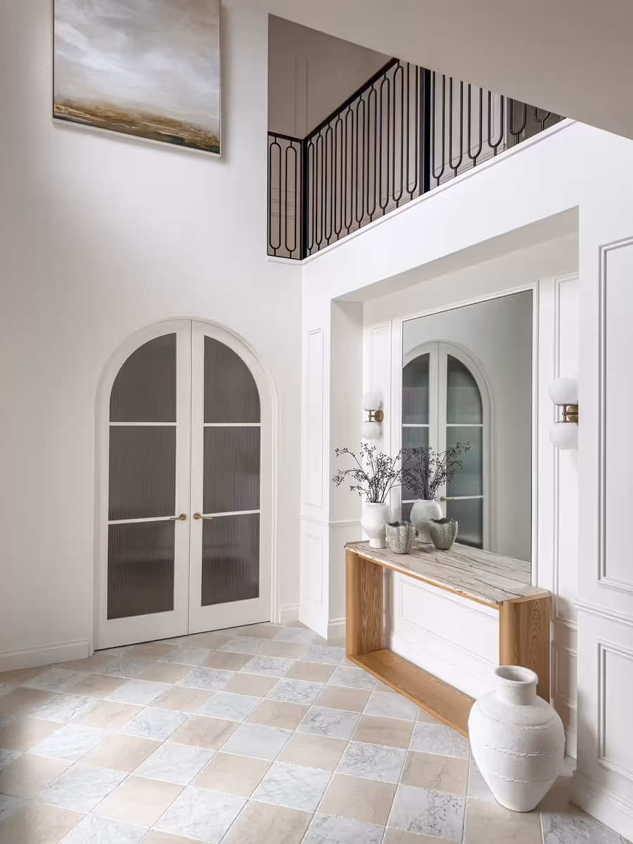 Double-height entry foyer with arched doors, an oak console and a checkerboard stone floor
