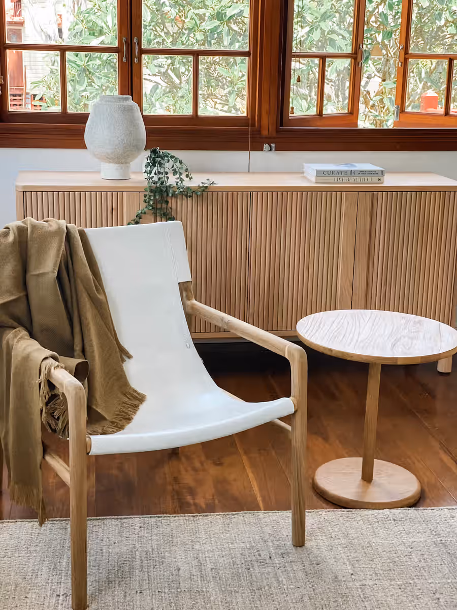 White leather sling chair beside a fluted timber sideboard, casement windows behind