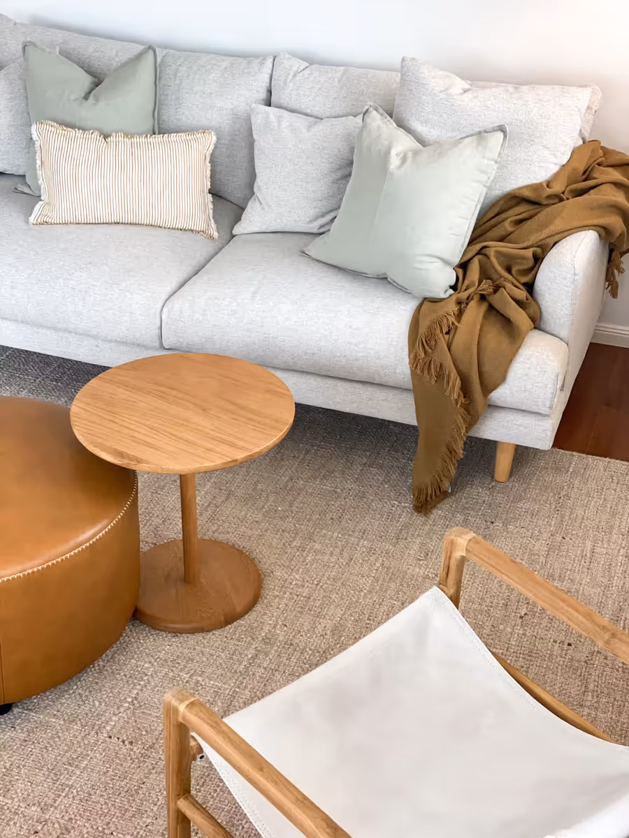 Pale sofa and a tan leather ottoman on a jute rug, with a round oak side table