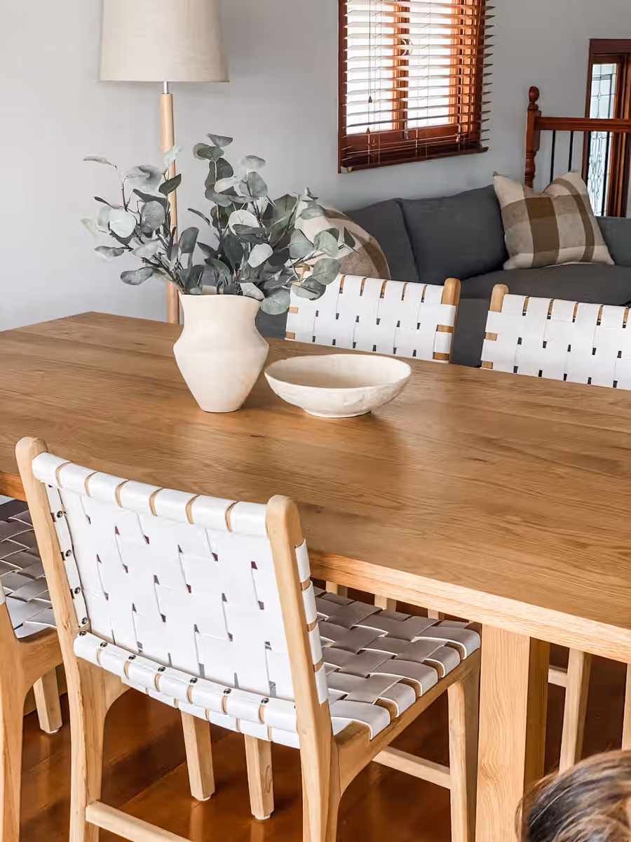 Oak dining table and woven leather chairs, with eucalyptus in a ceramic vase