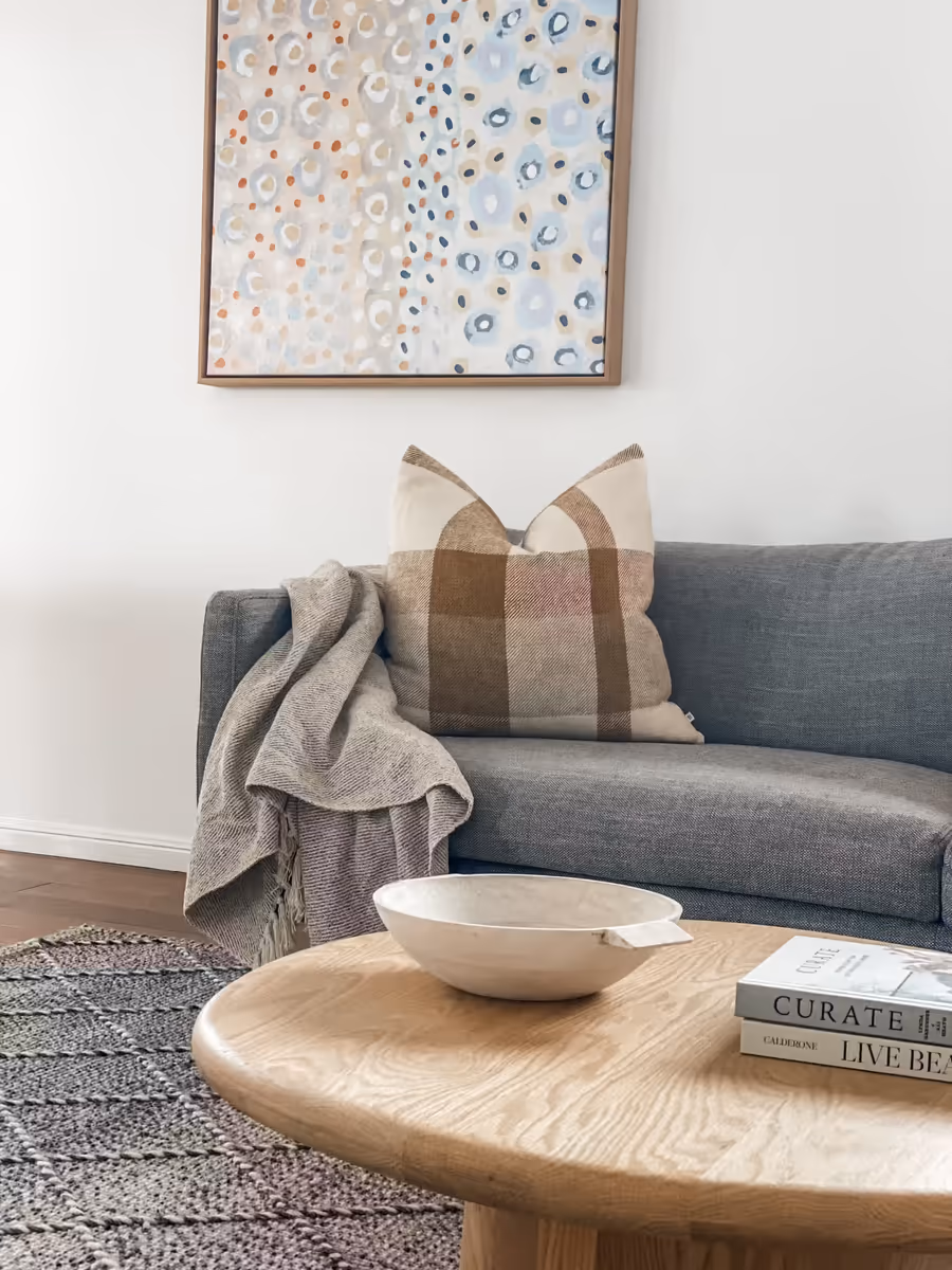 Grey sofa below a speckled abstract canvas, with a round oak table and a pale bowl