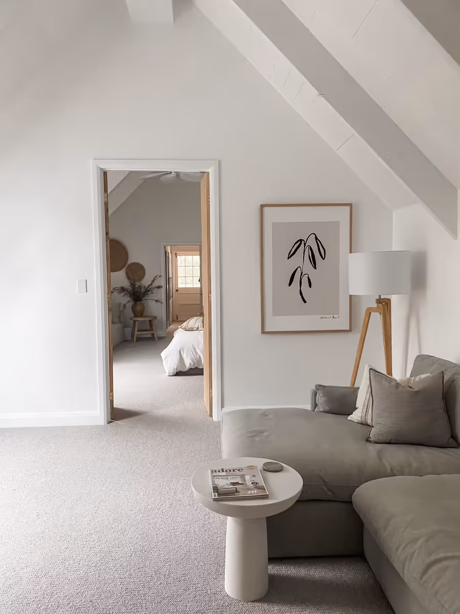 Sage sofa and a pedestal side table in the raked upstairs living room, bedroom beyond