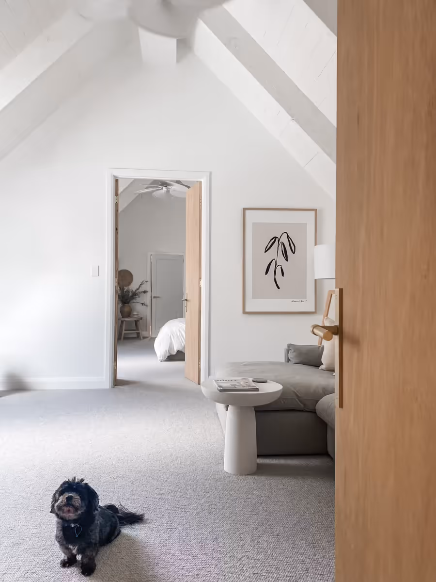 Oak door open onto the upstairs living room, with a small black dog on the carpet
