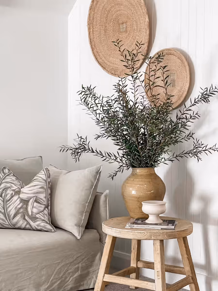 Olive branches in a terracotta urn beside the linen sofa, woven discs hung above