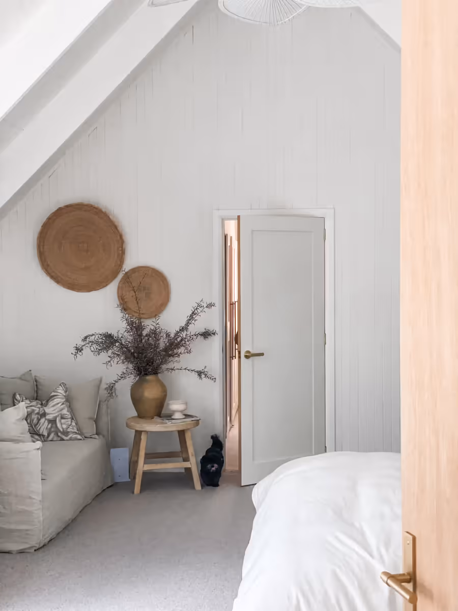 Woven wall discs above a timber stool of dried stems, the bed in the foreground
