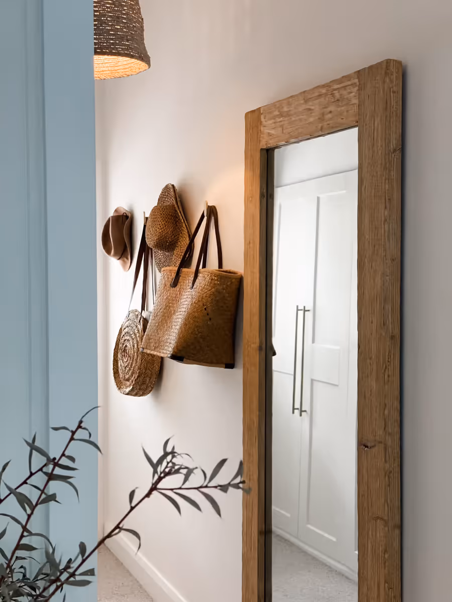 Straw hats and woven bags hung beside a full-length timber-framed mirror