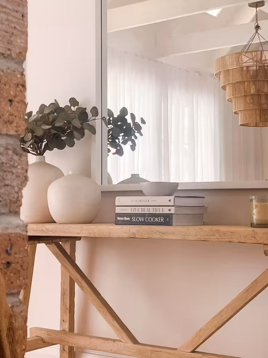 Timber console styled with ceramic vases and cookbooks against exposed brick
