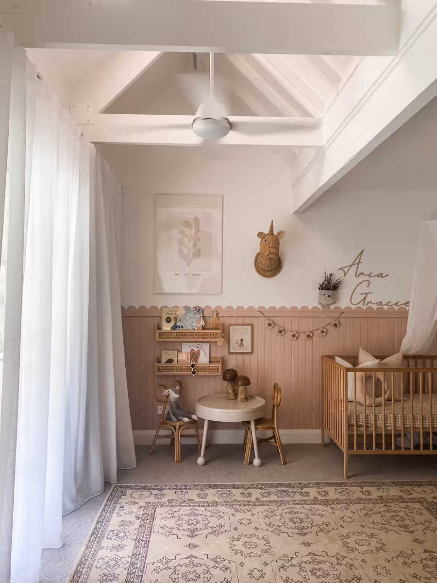 Nursery with blush scalloped panelling, a timber cot and a small table and chairs