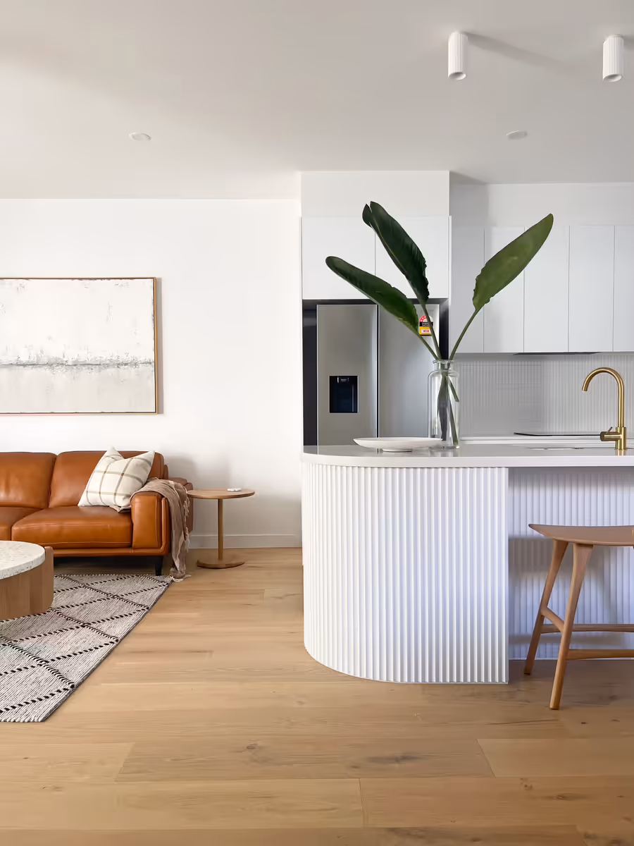 Tan leather sofa facing the fluted island bench, on wide oak floorboards