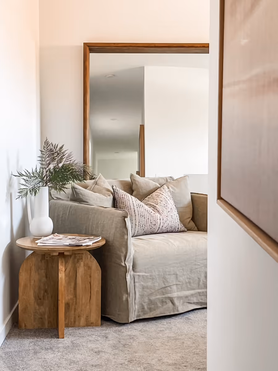 Linen sofa and a timber side table reflected in a tall floor mirror