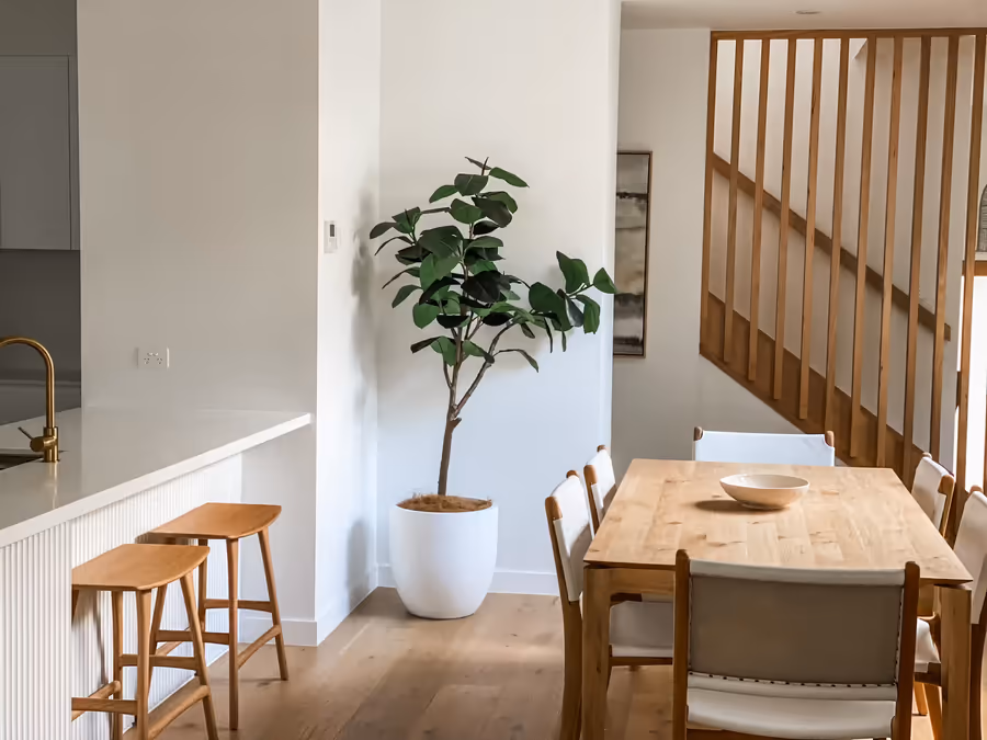 Dining table and chairs beside the fluted island, with a fig tree under the timber stair