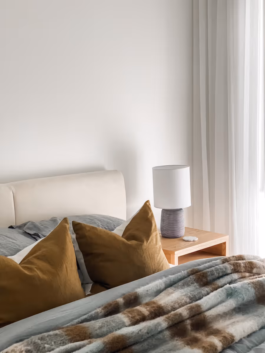 Curved bedhead with mustard cushions and a check throw, lamp on the oak bedside