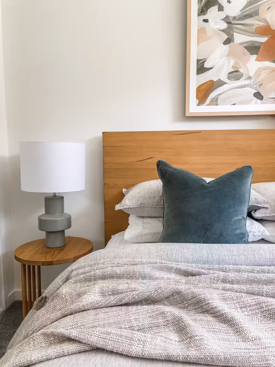 Timber bedhead with a teal velvet cushion, beside a round oak bedside table