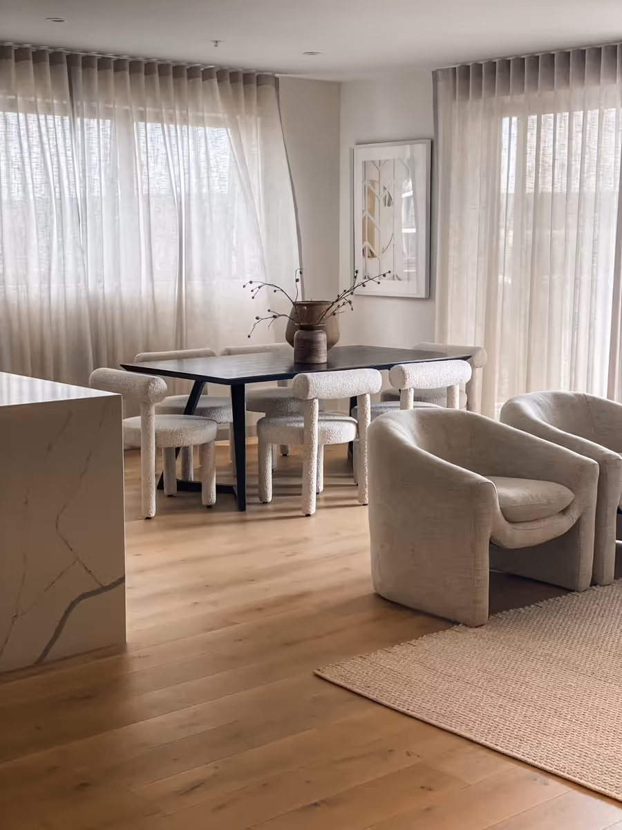 Black dining table and boucle chairs beside the stone island, sheers drawn behind
