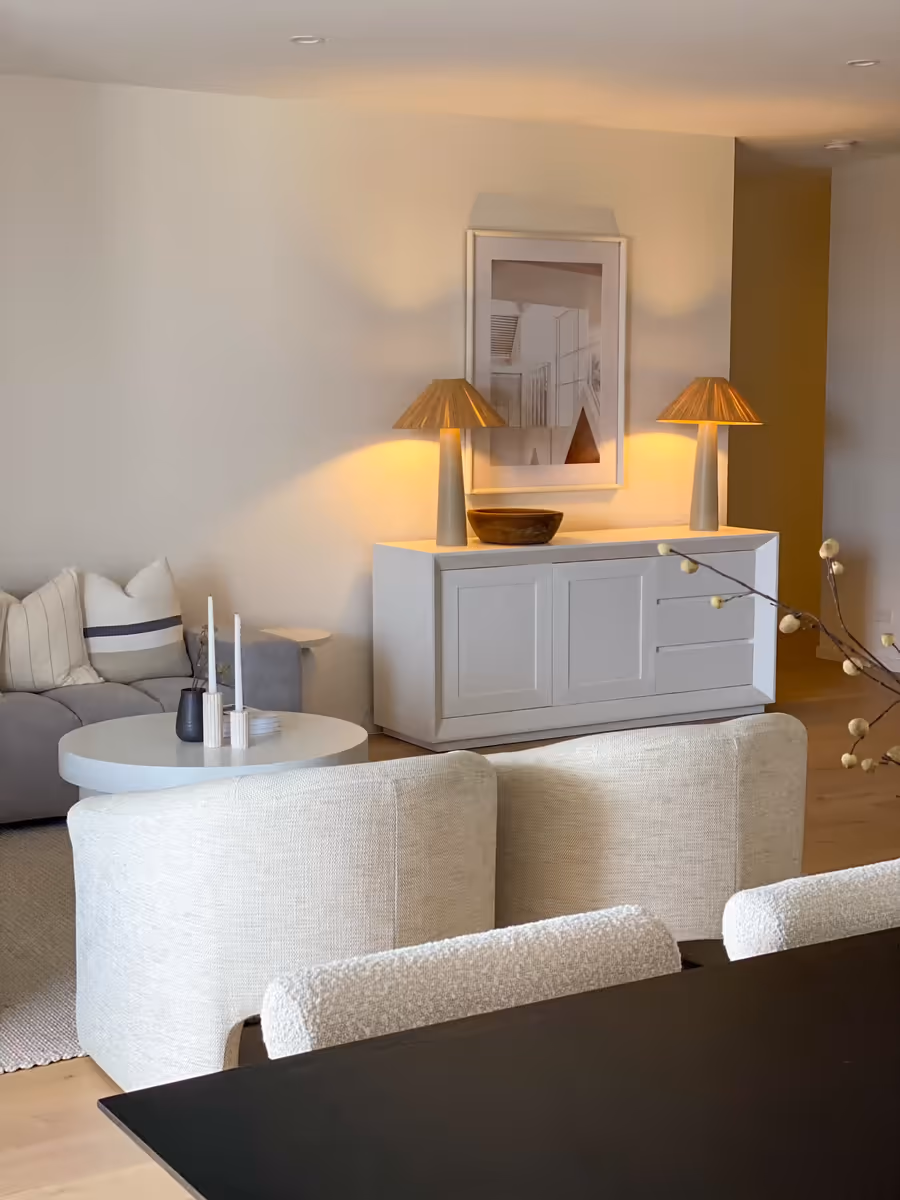 Lamps either side of a white sideboard, lit warm behind the boucle dining chairs