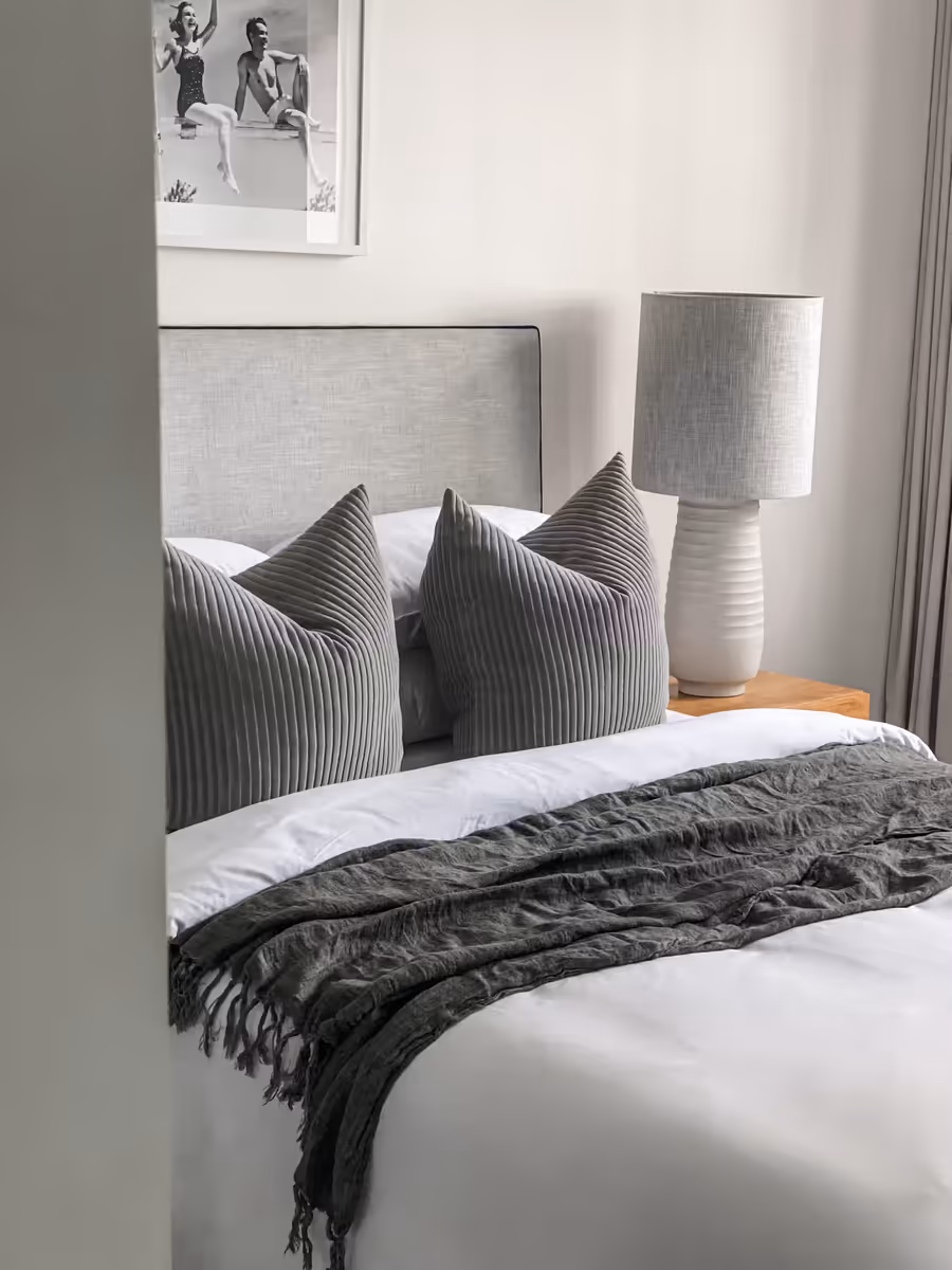 Grey upholstered bedhead with striped cushions and a charcoal throw