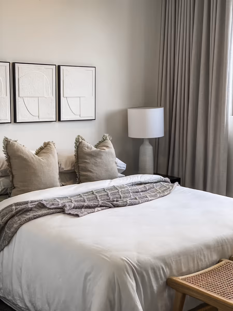 White bedding and fringed cushions below a trio of line-drawing prints