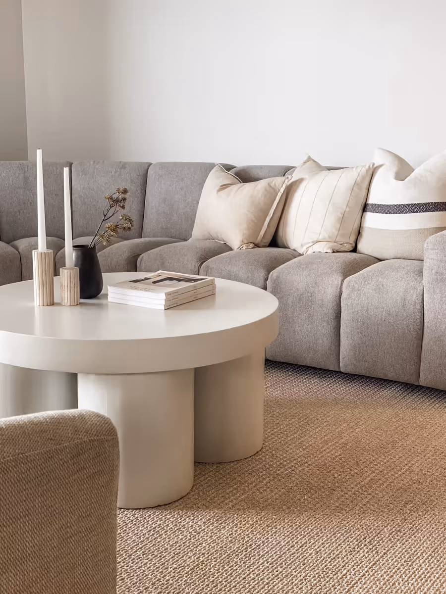 Round white coffee table with candlesticks and books, against the grey modular sofa