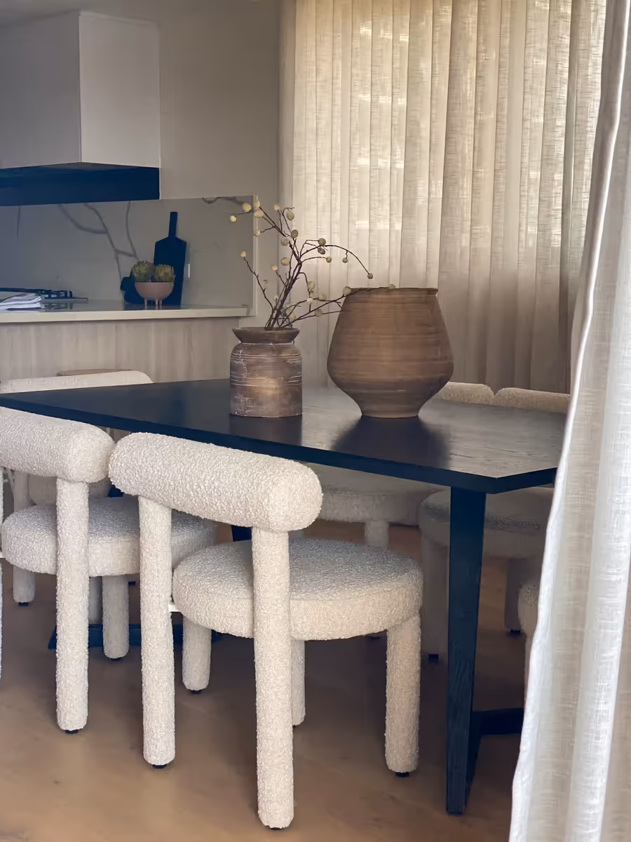 Turned timber vessels on the black dining table, boucle chairs pulled in around it